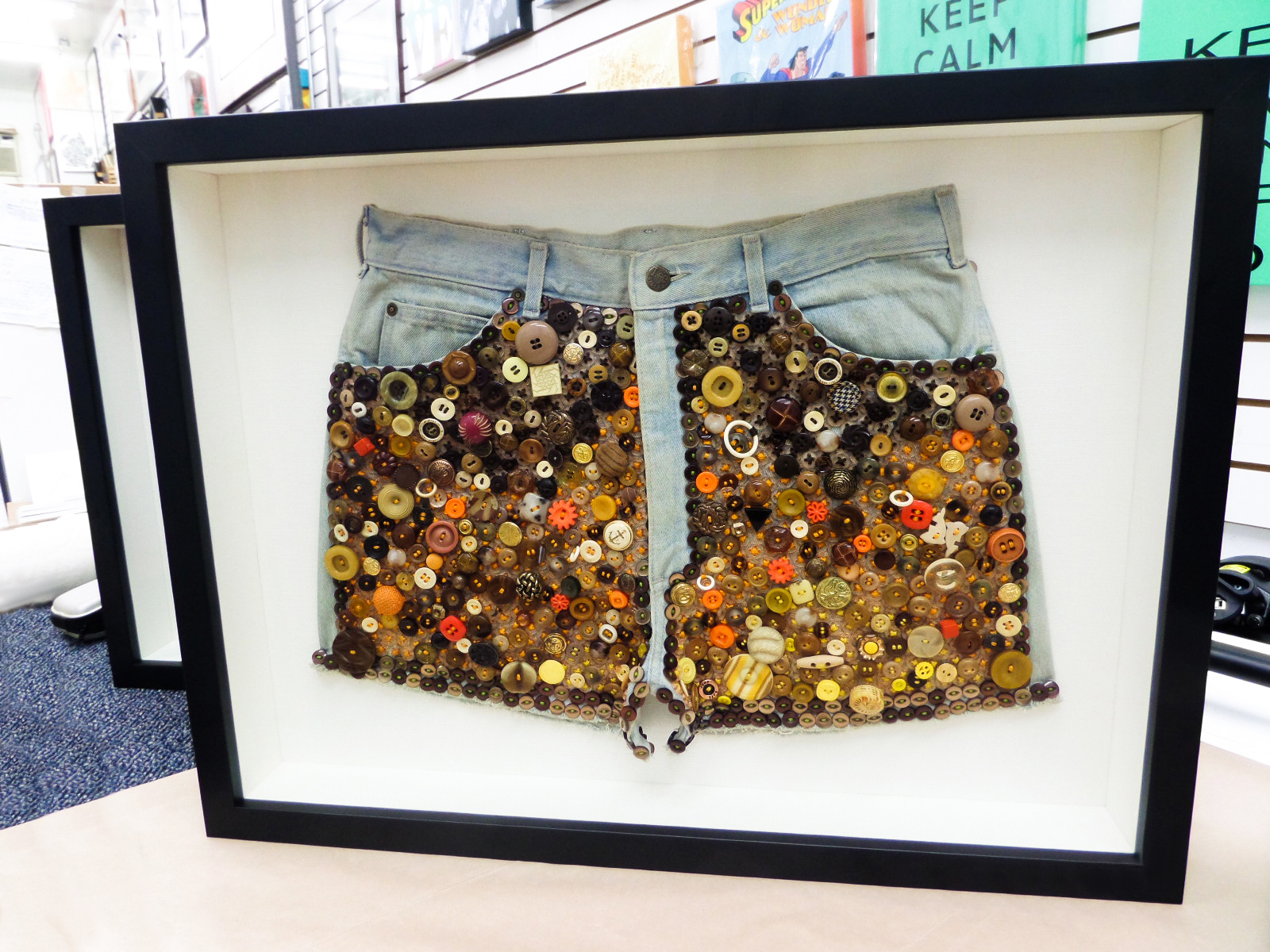 A denim shorts button-art piece in a deep shadow box